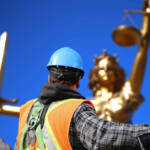 Operaio di schiena di fronte ad una statua dorata della giustizia